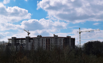 Crane - machine designed to lift and move in the cargo space, trawl, at the construction site against a blue sky with white clouds