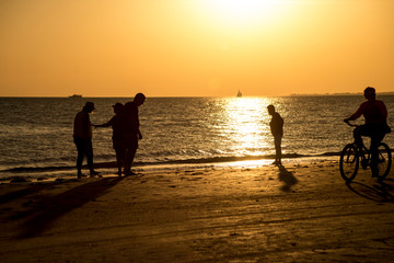 Silhouettes of people on an orange beach at sunset.