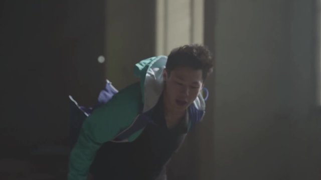 Young asian hip-hop street dancer dancing in the dark abandoned building in front of blue gas barrel. The man making moves and jumping. Slow motion