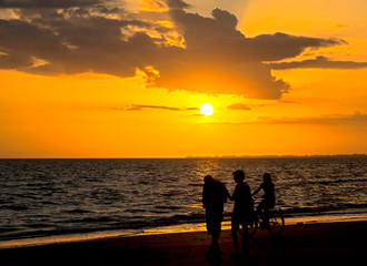 Fototapeta na wymiar Silhouettes of people on an orange beach at sunset.