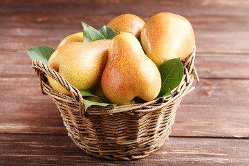 Ripe pears and green leafs in basket on brown wooden table