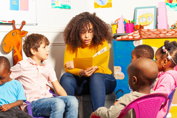 Teacher in nursery school reading a book to kids
