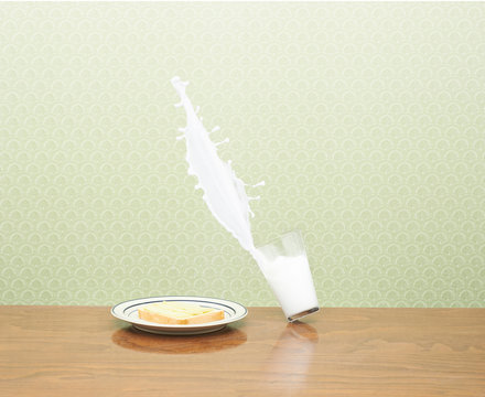 Milk spilling from glass besides breakfast plate on wooden table