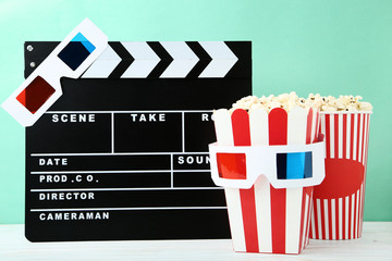 Clapper board with popcorn and glasses on mint background