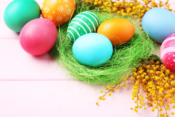 Fototapeta na wymiar Colorful easter eggs in nest with yellow flowers on wooden table