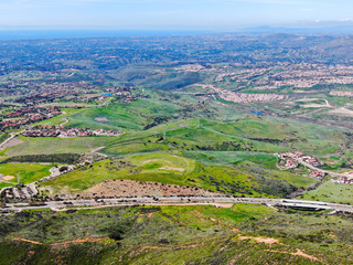 Naklejka premium Aerial view Black Mountain of Carmel Valley with suburban neighborhood and identical villas next to each other on the back, San Diego, California, USA. Green dry valley during sunny cloudy day.