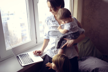 Mom with children working on laptop near window
