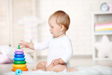 Naklejka premium Baby boy with toys sitting on carpet at home