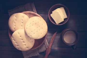 Traditional Chilean Hallulla bread rolls on wooden plate with butter and coffee with milk on the...