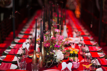 Table wedding decor in red and black tones. Pink, blue and red flowers bouquet and candles in bottles.