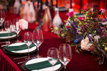 Table wedding decor in red and black tones. Pink, blue and red flowers bouquet and candles in bottles.