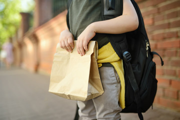 Student with big backpack and lunch bag near the school building. Hands and lunch bag close-up.