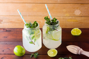 Mojito and mint on wooden background. Refreshing cocktail with lime and fresh mint on wooden boards. Two jars with handles with a summer drink with citrus and ice. Homemade mojito