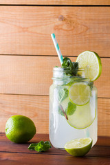 Mojito and mint on wooden background. Refreshing cocktail with lime and fresh mint on wooden boards. Two jars with handles with a summer drink with citrus and ice. Homemade mojito