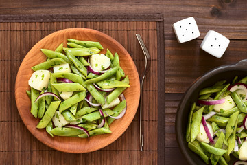 Green bean, potato and red onion salad with parsley served on wooden plate, photographed overhead on dark wood with natural light