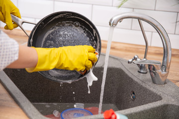 Female hand washing frying pan. Young housewife woman washing griddle in a kitchen sink with a sponge, Hand cleaning, manually, by hand, housework dishwasher