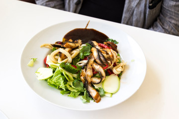 Salad with cilantro and fried eggplants in a white plate on a white table. In the background is a human figure.