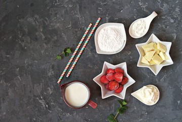 Fototapeta na wymiar Ingredients for the preparation of a dessert or drink : white chocolate, frozen strawberry, powdered sugar, milk, corn starch, fresh mint and whipped cream for decoration, straws. Top view, copy space