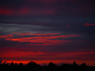 Dramatic sunset sky over small town silhouette. Rich red and blue tones.