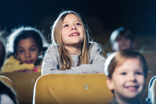 selective focus of cute smiling child watching movie together with multicultural friends