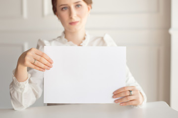 Woman holding white business card on white wall background.