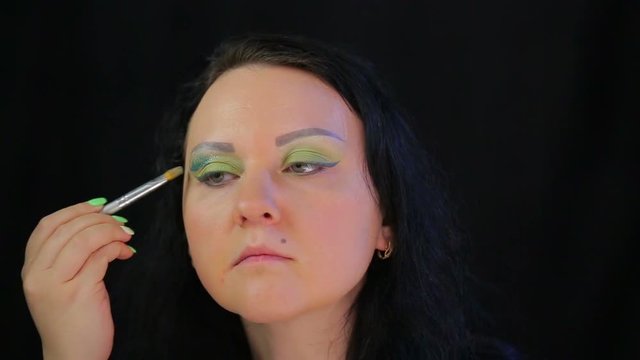 Brunette woman applies juicy green sparkles on eyelids.