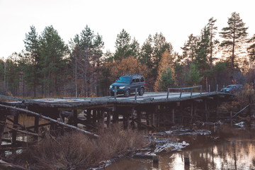 Fototapeta na wymiar SUV moves on a wooden bridge over a river in the forest