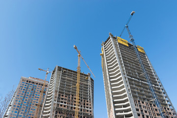 Fototapeta premium high-rise construction crane with a long arrow of yellow color against the blue sky over a new multi-storey building of concrete and brick under construction