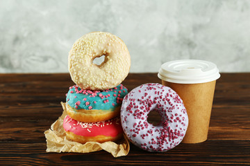 Vibrant composition of lush donut with colorful sprinkled icing and disposable paper cup on wood textured background copy space for text. Tasty but unhealthy food concept. Close up, flat lay, top view