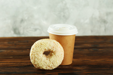 Vibrant composition of lush donut with colorful sprinkled icing and disposable paper cup on wood textured background copy space for text. Tasty but unhealthy food concept. Close up, flat lay, top view