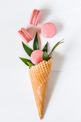 Spring abstract bouquet with a waffle cone, coral macaroons and green plant on a white background. Top view, flat lay.