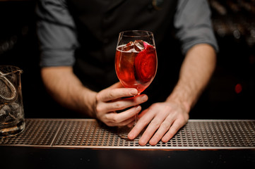 Red cocktail in glass in bartender's hands