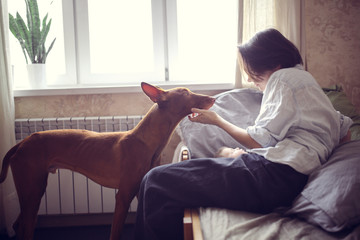 Woman hugs Pharaoh's dog on floor in apartment