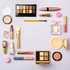Square image of cosmetics for social media with empty place for text. Woman make up cosmetics on purple. Copy space. Gold and purple decorative cosmetic: highlighter, concealer, rouge, eye shadows etc