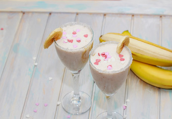 Homemade Banana smoothies or cocktail on wood table in two glasses decorated with piece of banana decorated with sugar hearts
