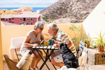 couple of aged gentlemen and lady drinkk together fruit juice on rooftop terrace wih two funny pug dog under the sunlight. amazing ocean view for great retired concept