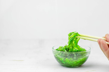 Green wakame seaweed salad in some transparent glass bowls, on a white wooden table