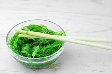 Green wakame seaweed salad in some transparent glass bowls, on a white wooden table