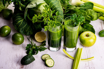 Green smoothie with fruits and vegetables on white wooden background.