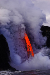 Hot lava flows from high cliff into the ocean in Big Island in Hawaii
