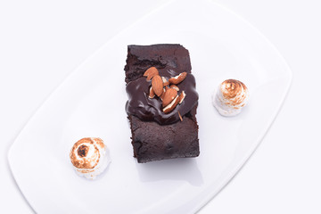 Delicious chocolate cake on a white plate close-up with small bize and whole almond nuts