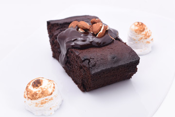 Delicious chocolate cake on a white plate close-up with small bize and whole almond nuts