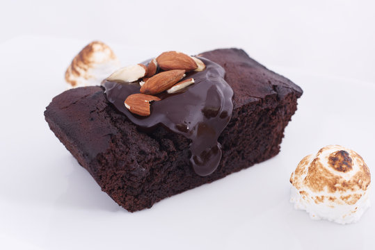 Delicious chocolate cake on a white plate close-up with small bize and whole almond nuts