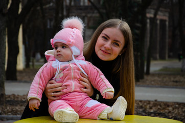 Mom plays on a bright playground with a small child in the street, nomads, a house during the day