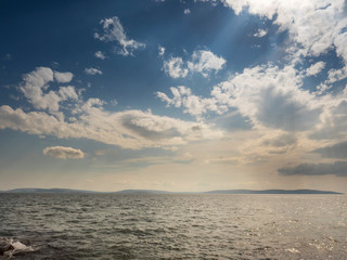 Atlantic ocean surface, Galway bay, Burren mountains in the background, cloudy sky, simple  seascape, blue dominant color.