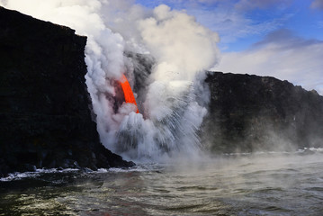 Hot lava flows from high cliff into the ocean in Big Island in Hawaii