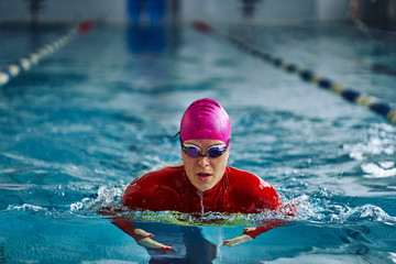 Female athlete in a red-yellow swimsuit is swimming in the style of breaststroke. Splashes of water...