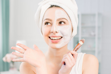 Happy and emotional Spa girl applying face mask. Aesthetic procedure. The girl applies an anti-aging mask of clay on half of the face with a brush