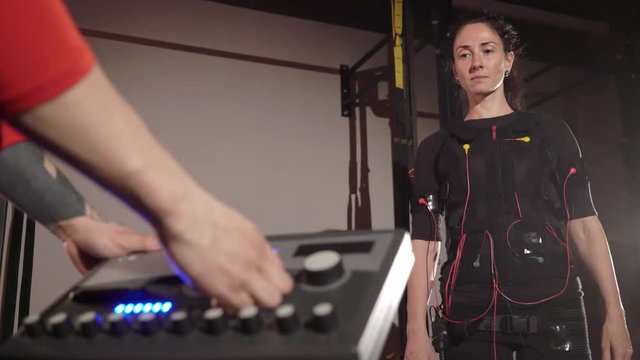 EMS electro stimulation sports equipment in gym. Trainer and woman doing exercises