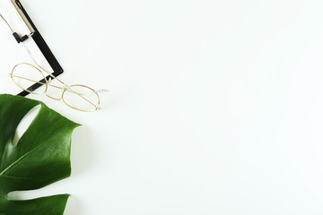 Female blog writer workspace concept. Big green monstera palm leaf on femenine desktop composition. Background, close up, copy space, flat lay, top view.